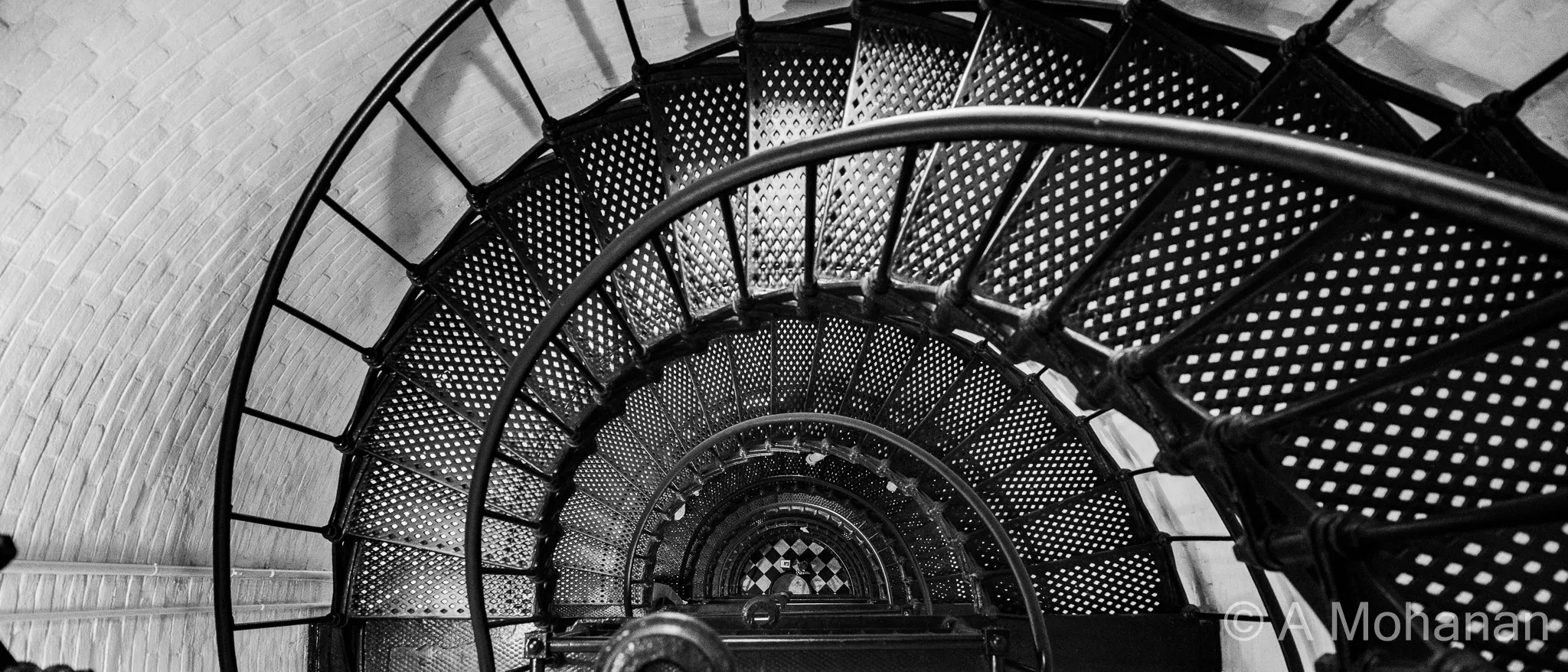 Looking straight down the cast iron spiral staircase of St. Augustine Lighthouse, perforated diamond-pattern treads forming hypnotic concentric rings.